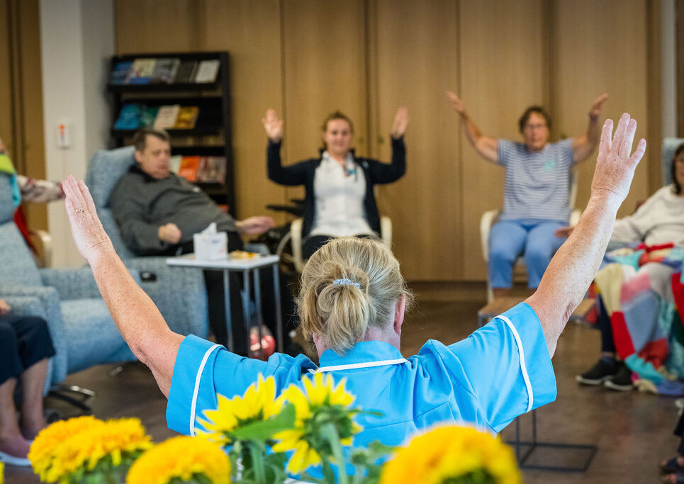 A group of patients, staff and volunteers do a seated tai chi session in the Living Well Centre at St Richard's Hospice