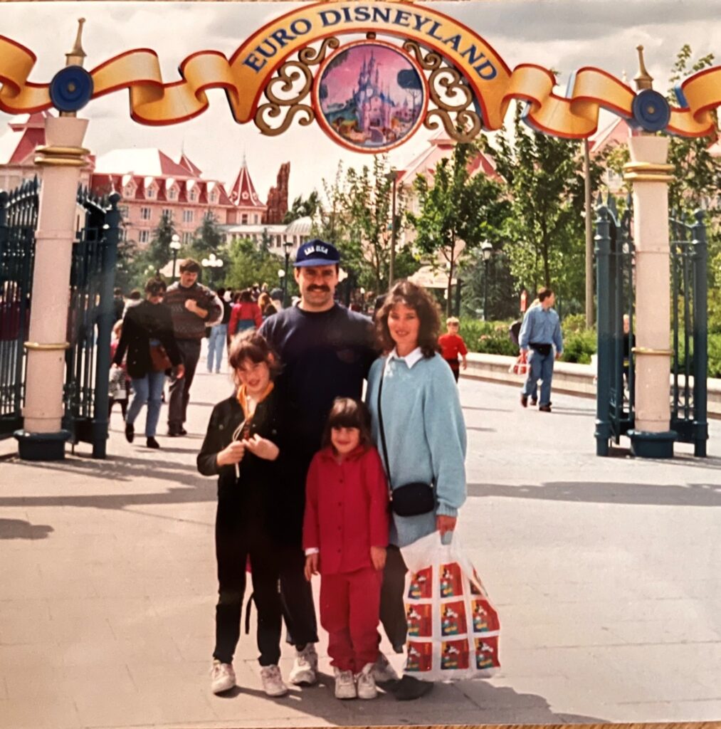Two children with parents standing in front of an arch with the sign Euro Disneyland in 1994