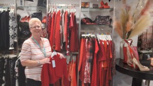 Sandy standing in front of a row of mainly  red clothing items in the shop