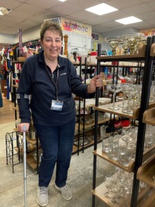 Shop volunteer Tracy stands in the store next to shelves of glassware