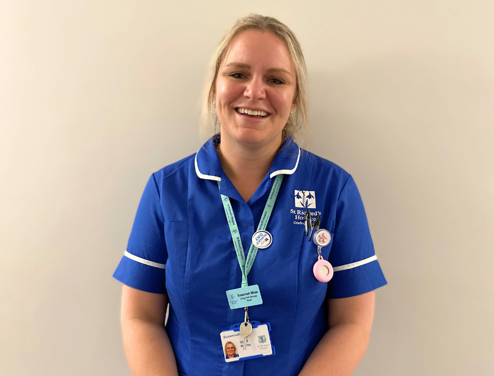 Susannah pictured in front of a plain white wall. She is smiling and wearing her blue nurses' uniform.