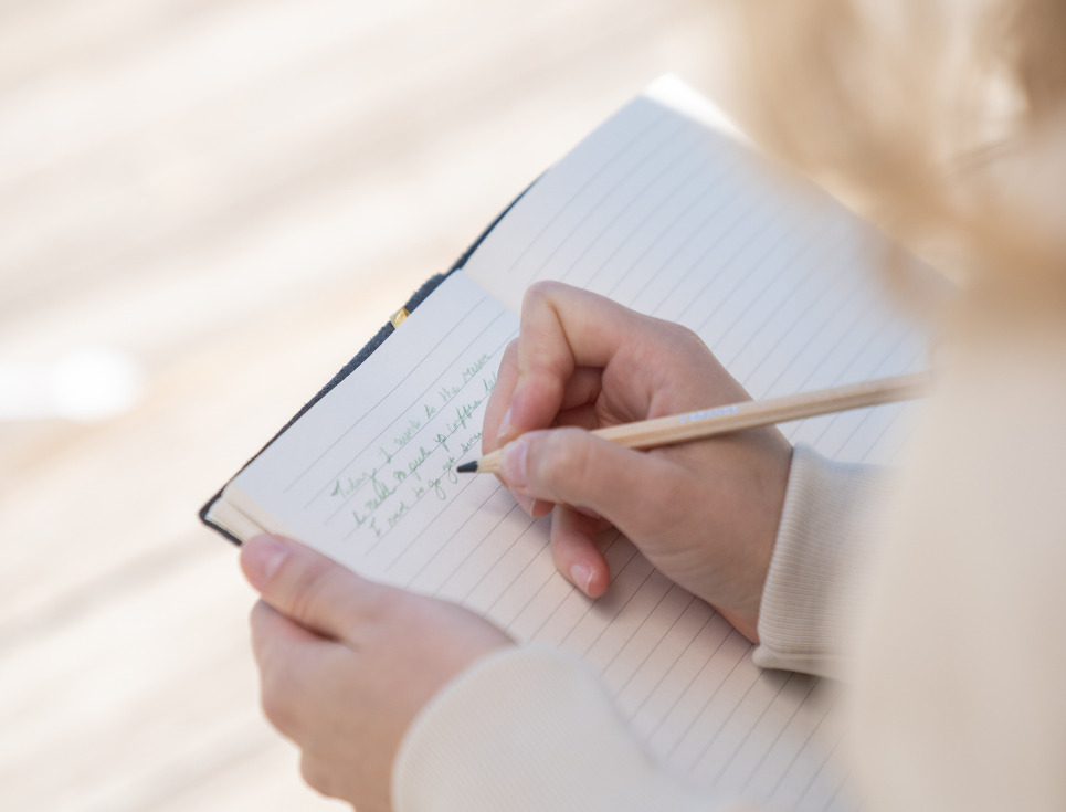 A close-up photo over a person's shoulder as they write into a journal.