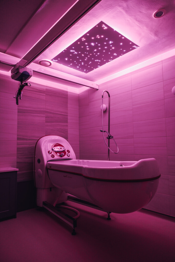 A Jacuzzi bath lit up with purple lights. A panel on the ceiling glitters with twinkling lights. 