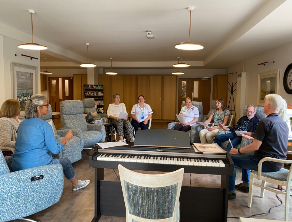 A group of people seated in the Living Well Centre with two volunteers leading the group