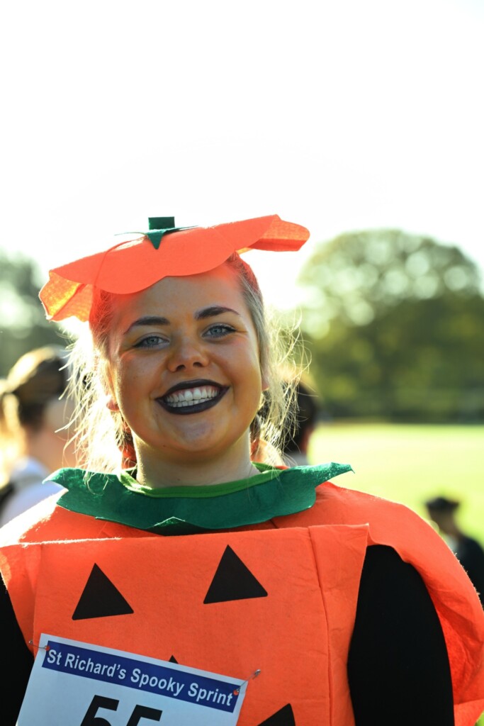 A woman dressed in a bright orange pumpkin costume smiles at the hospice's Spooky Sprint.