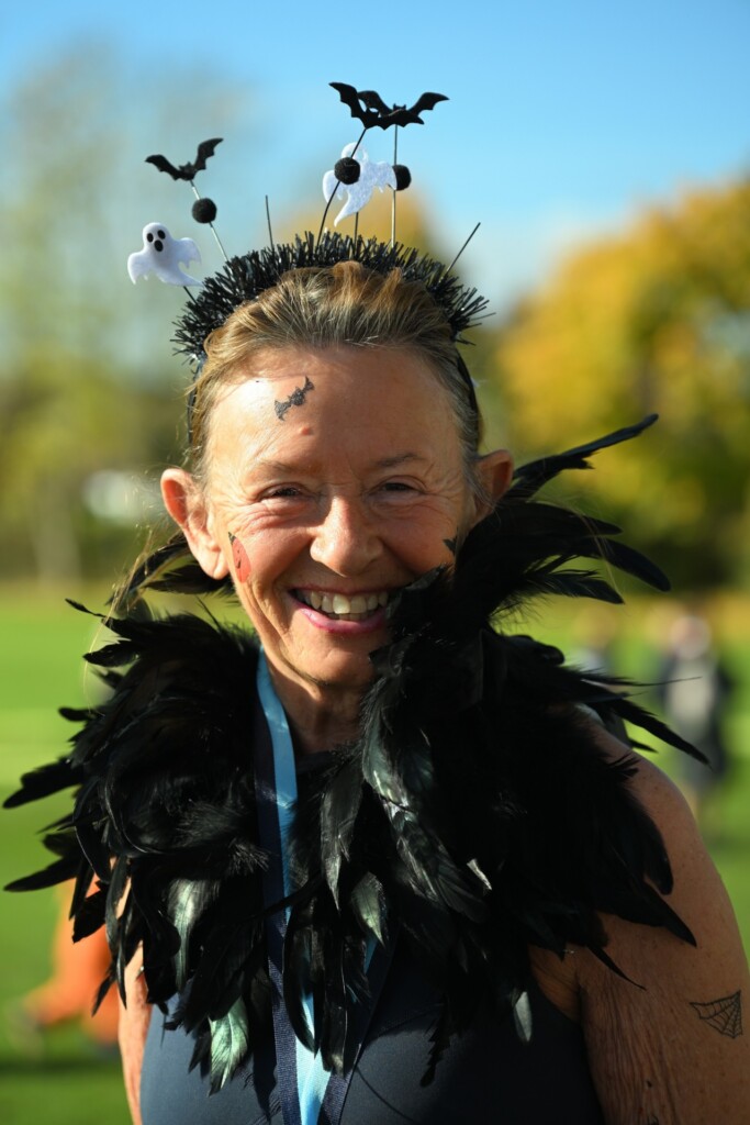 A woman dressed in a black feathered scarf and wearing a headband decorated with ghosts and bats smiles at the hospice's Spooky Sprint event.