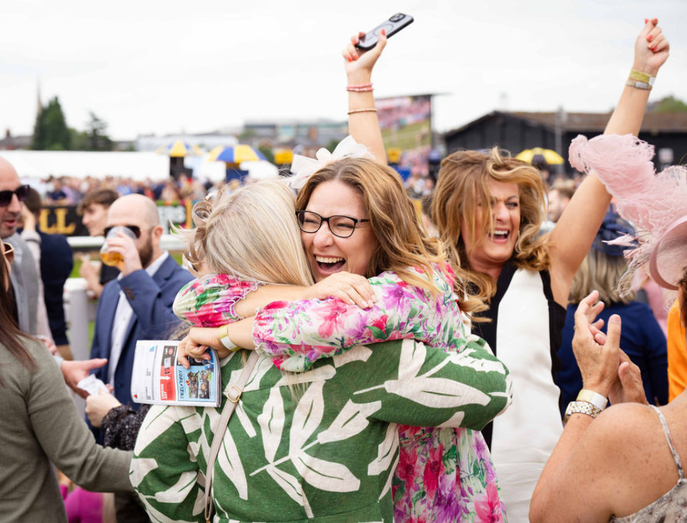 Two women embracing jovially as they have won on the races.