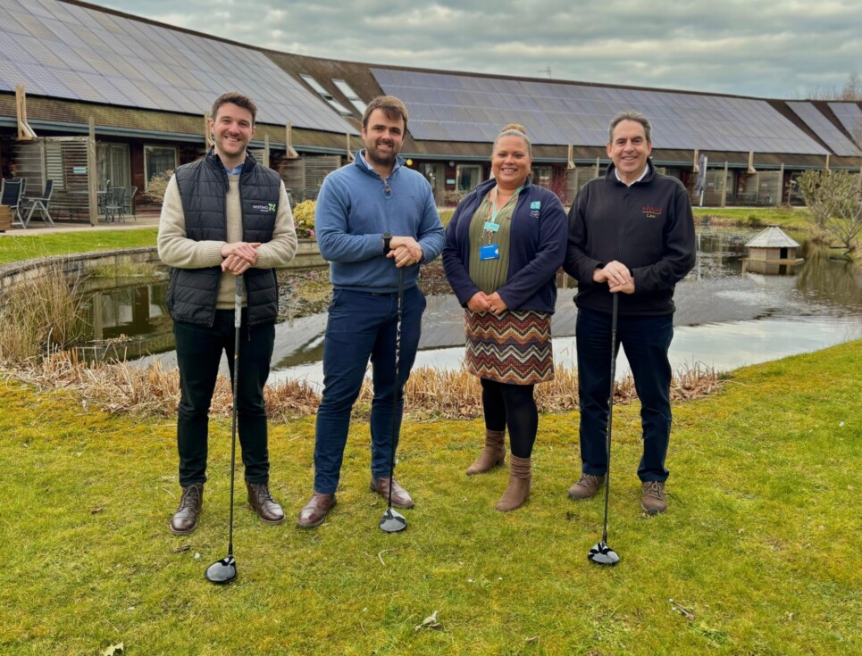 Four people, three of who are holding golf clubs, stand together in the gardens at St Richard's Hospice.