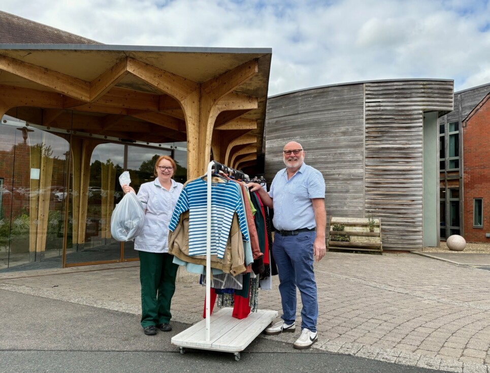 A hospice occupational therapist and retail team member stand outside the hospice building with a rail of clothing