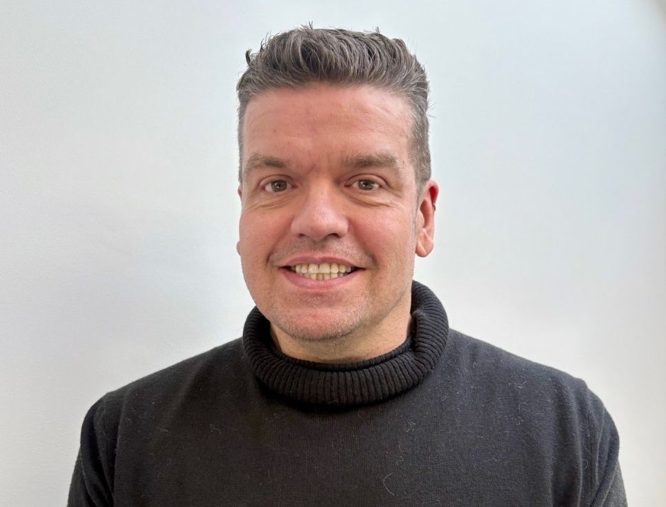 Andy pictured wearing a black roll-neck jumper. He is smiling and has short dark hair.