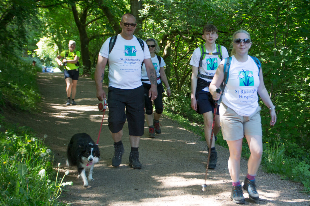 Group of people walking along a woodland path wearing St Richard’s Hospice T-shirts, with one person leading a dog on a lead.