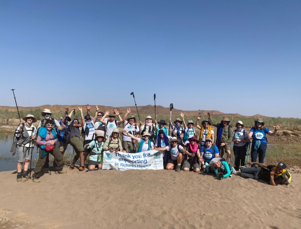 Fundraisers for St Richard’s Hospice pose with a thank you banner beside a river in a desert landscape after completing a trekking challenge.